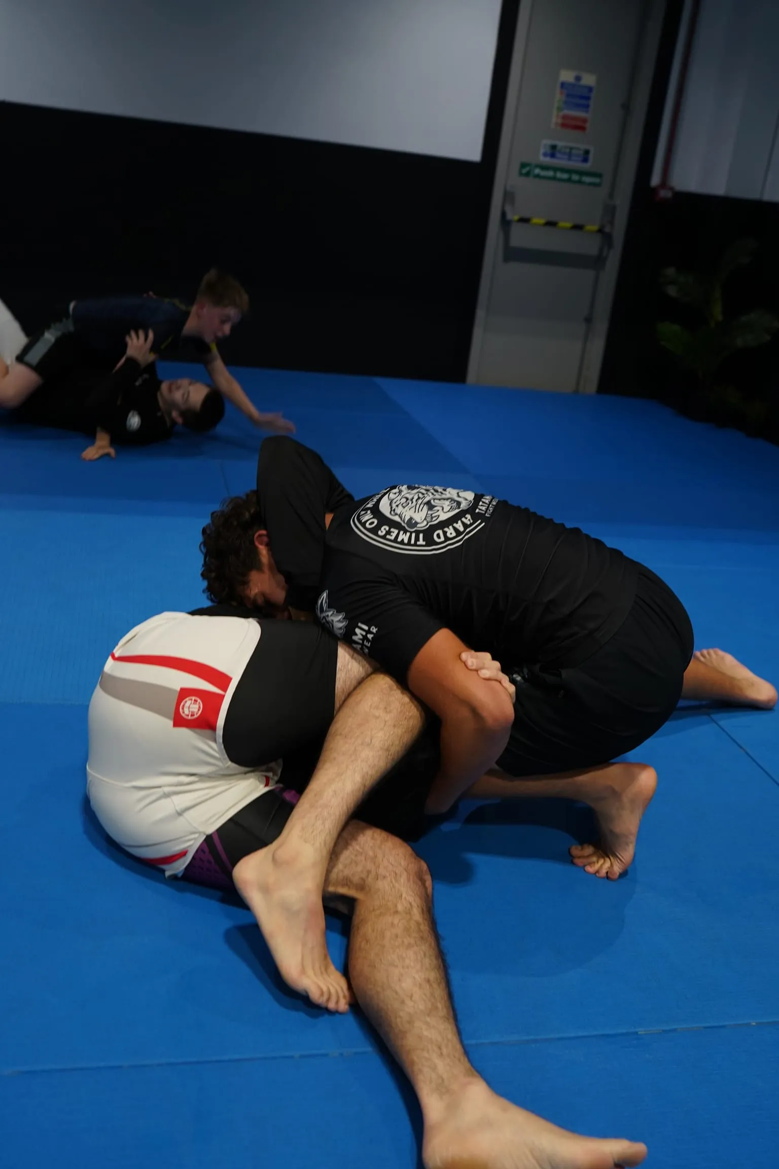 Two members grappling on the mat during a positional round at Rebel Combat Sports, with another pair training behind them