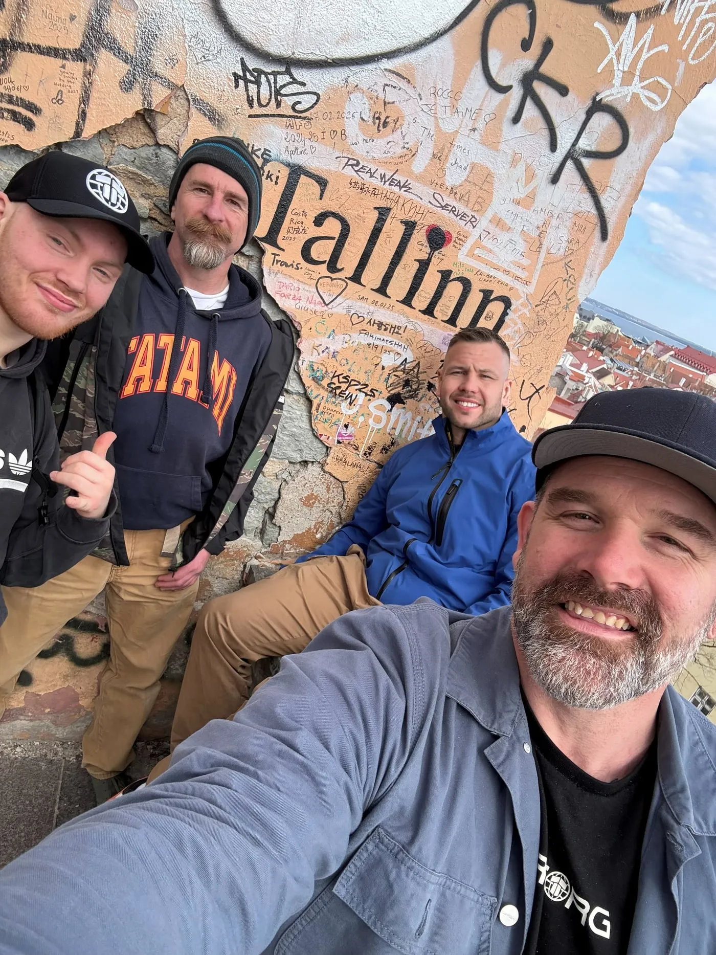 Four grapplers taking a selfie against a graffiti-covered wall reading Tallinn, on a trip to a BJJ Globetrotters camp
